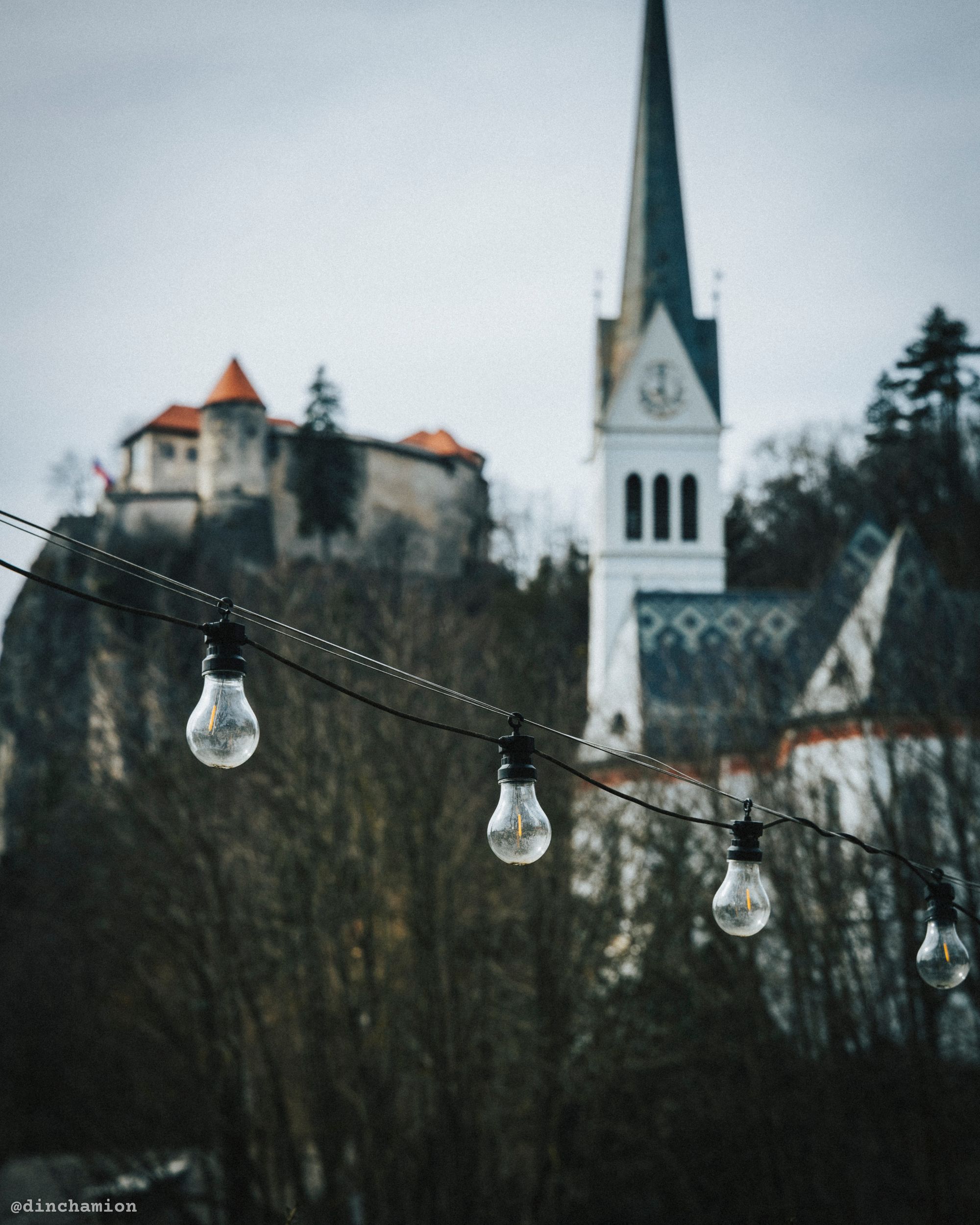 A decorative string of lightbulbs with Bled Castle and the St. Martina Parish Church in the background.